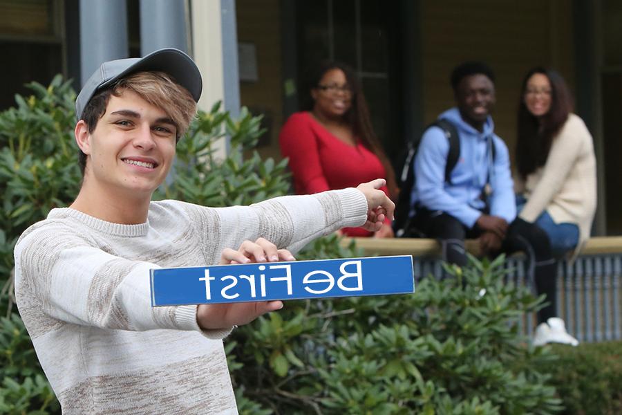 first-generation student smiles and holds a sign that reads Be First.